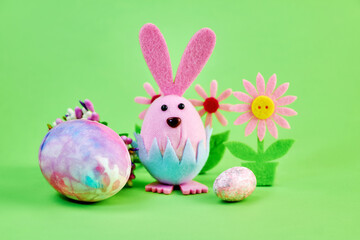 funny toy pink rabbit celebrates Easter with big and small colorful eggs and flowers on a green background