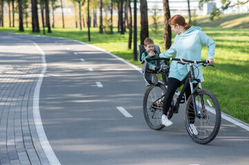 Caucasian woman riding a bicycle with her toddler son sitting behind her in a child seat. 