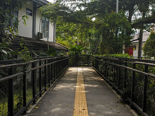 Stone block paths and yellow guide blocks with iron railings in lush gardens, details of a botanical garden.