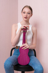 Portrait of calm young female musician with ukulele held upright, sitting on bar stool and looking...