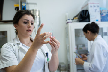 A focused nurse in a white lab coat carefully prepares a syringe for an injection in a professional...