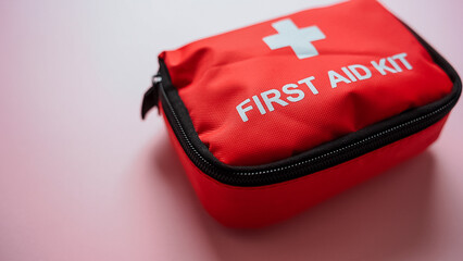 A bright red first aid kit is currently positioned on a soft pink surface, ready for any potential emergencies that may arise, providing essential health care support whenever needed