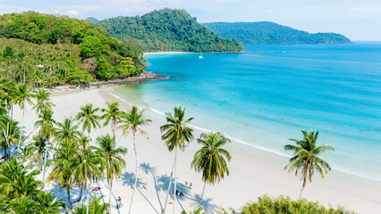 Soft white sands meet the vibrant turquoise waters of Koh Kood Island, Thailand, bordered by lush green hills. Palm trees sway gently in the tropical breeze, creating a serene paradise.
