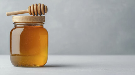 glass jar filled with golden honey sits on gray surface, accompanied by wooden dipper resting on top, creating simple and inviting scene