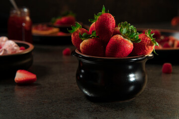 black ceramic pot filled with strawberries in the foreground against a background of plates with strawberry desserts