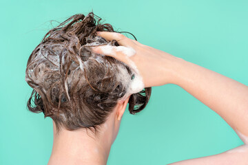 Naklejka premium A woman washes her hair with shampoo on mint background, rear view.