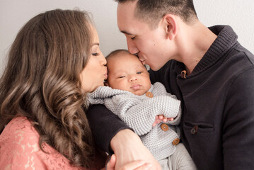 Parents kiss baby’s cheeks while holding them lovingly in arms