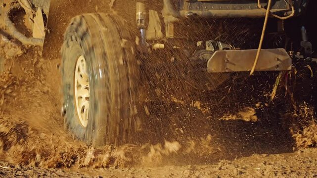 An off-road vehicle driving through a muddy puddle, water and mud splashing around in all directions. Close-up of wheels and suspension of the car. Front view. Slow motion