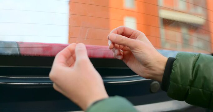 Close up of hands applying static sticker to car rear window during dash cam installation