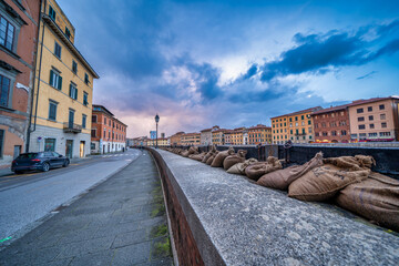 Dramatic view of the swollen Arno River at sunset with flood defenses along Pisa’s Lungarni