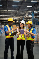 Three workers in safety vests are standing in a warehouse, pointing at something on their tablets....