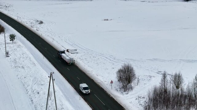 Tractor towing trailer with hay over country road in winter season, aerial view