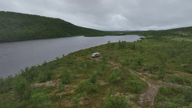 Drone view of a van in the vast green landscape of Masi,  Norway, near calm waters
