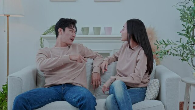 Asian couple arguing on sofa at home, husband blaming upset wife, family conflict concept
