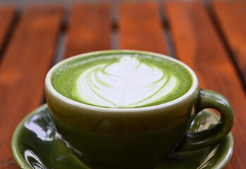 Photo of hot tea matcha with latte art with spoon in a green cup on wooden table. Copy space for text. Close up. Green. blur, bokeh.