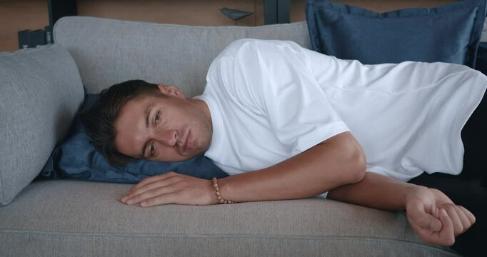 Apathetic bored man falls down on sofa at home alone. Depression concept. Tired man lying asleep feeling out of energy motivation. Depressed tired male feeling lack of motivation after hard day work