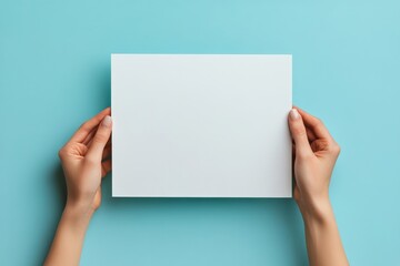 Female hands holding blank white paper sheet on light blue background. Top view. Mockup paper with copy space for text