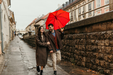Mid aged couple walking under red umbrella on rainy autumn day