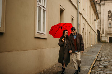 Happy couple walking under red umbrella during rainy day in the city