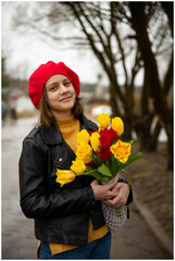 Portrait of a 13-year-old teenage girl in a red beret with a bouquet of tulips in a spring park