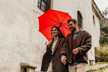 Romantic couple walking and sharing a moment under a red umbrella