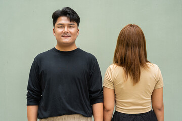 Fototapeta premium Portrait of young couple against plain wall while other person is facing the wall