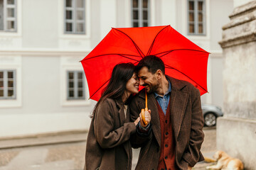 Happy couple holding red umbrella and smiling on a rainy day
