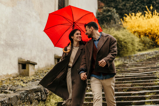 Happy couple walking under red umbrella on rainy day