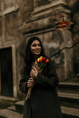 Young woman holding tulips is smiling near an old building