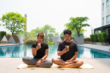 young couple doing yoga next to pool and using phone