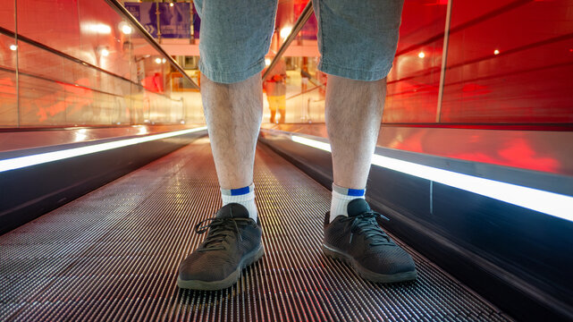 A man stands safely on a moving walkway or escalator, with proper positioning&mdash;feet placed firmly and centered&mdash;demonstrating essential safety practices to maintain balance and avoid potential accidents
