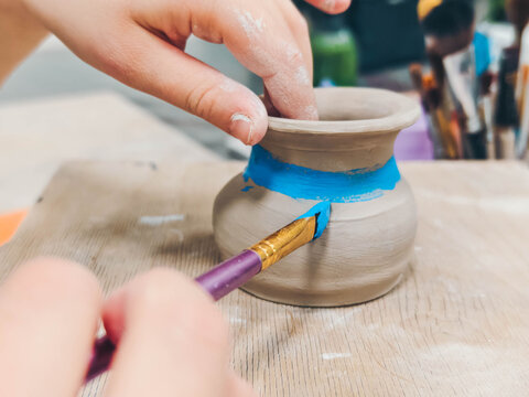 Child paints a vase in a pottery workshop. Creativity and traditional crafts concept. 