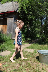 Little girl in a swimsuit in the garden coming to the basin. 