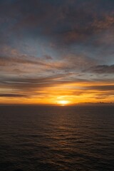 Fototapeta premium stunning sunset over ocean. horizon is painted in warm shades of orange and gold, reflecting on surface of water. sky is covered with picturesque clouds that create smooth gradients of light shadow.