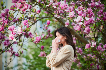 Woman allergic suffering from seasonal allergy at spring in blossoming garden at springtime. Young...
