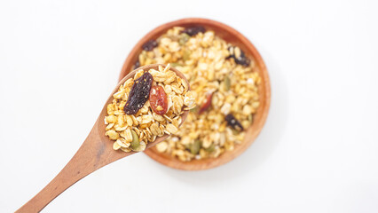 Crunchy granola with assorted oats, nuts, and dried fruits on wooden plate and spoon isolated on...