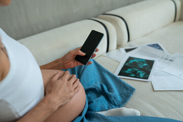 Pregnant woman consults with doctor through smartphone, holding ultrasound scan and test results. Telemedicine from home, assistance to patients with remote medical consultation