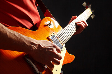 Guitarist in red with orange electric guitar on dark stage.