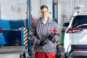 Caucasian young male auto mechanic holding wrench in car repair shop