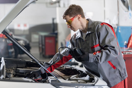 Mechanic man is measuring battery power of suv car by battery tester at service