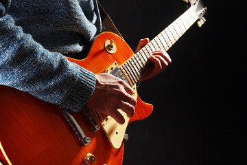 Musician in blue sweater with orange electric guitar on dark stage.