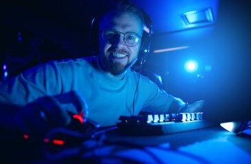 Enthusiastic happy man gamer engaged in online gaming at night with headset