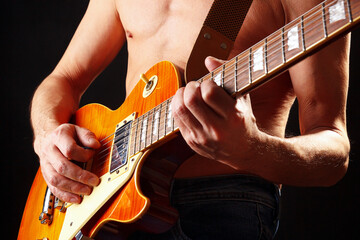 Musician with orange electric guitar on dark stage.