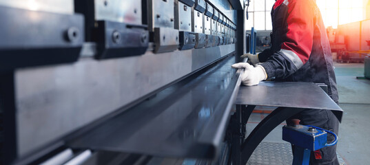 Male worker operating industrial metal press brake in factory setting, banner