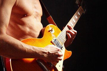 Rock guitarist plays the orange sunburst electric guitar on dark stage.