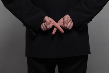 Businessman in black suit crosses his fingers behind his back. Concept of corporate espionage, fraudulence and fake agreements