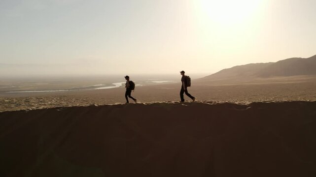 Two female sporty hikers walking on top of a sand dune on sunset in the Altyn Emel national park, Kazakhstan