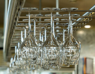 Group of wine glasses hanging upside down above a bar rack in pub or restaurant. Glasses for wine on a bar with serving items.