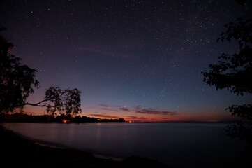 A mesmerizing starry night captured with long exposure, showcasing star trails over a calm lake...