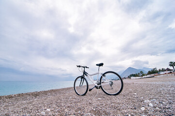 Fototapeta premium White Bicycle on Rocky Beach with Ocean and Mountain Background..